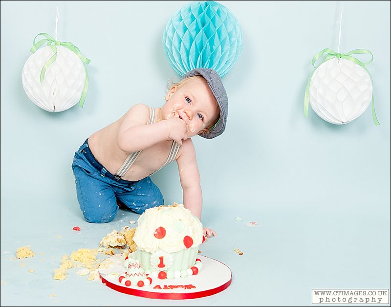 baby boy cake smash, flat cap, braces, baby eating cake, blue backdrop,